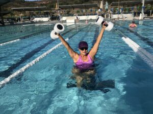 An active Hispanic Latin woman does water aerobics in the pool.