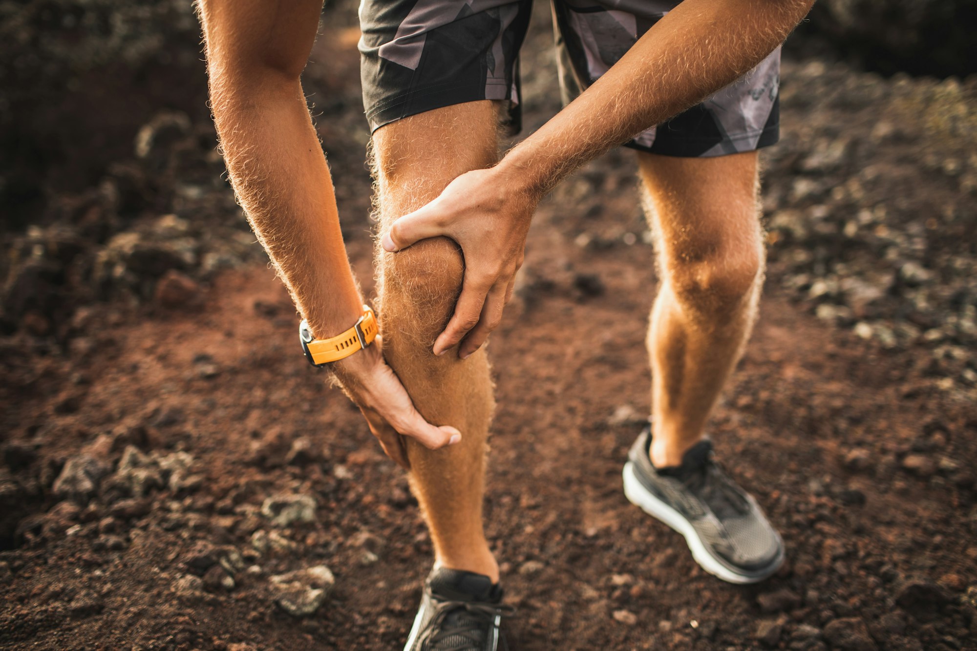 Knee injury on running outdoors. Man holding knee by hands close-up and suffering with pain